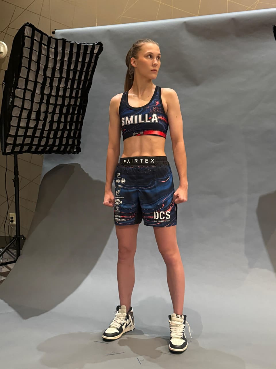 Smilla Sundell standing for a portrait session in a black "Smilla" branded fight kit and high-top sneakers