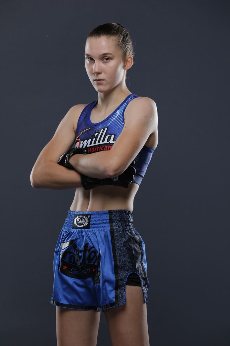 Studio portrait of Smilla Sundell standing with her gloved arms folded, in a blue "Smilla The Hurricane" top and blue Fairtex shorts